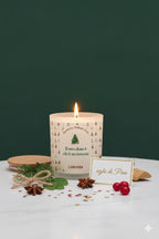 Candela artigianale Luminah alla fragranza Aghi di Pino accesa, con elementi naturali natalizi su sfondo verde.