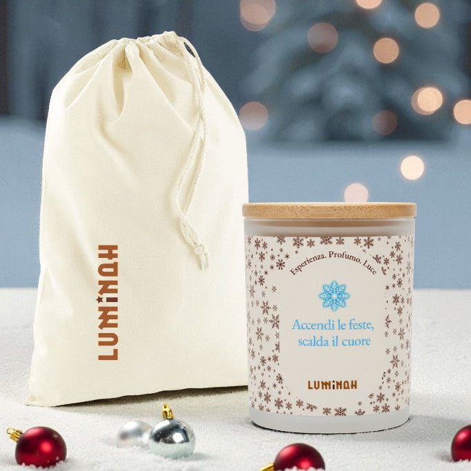 Candela Luminah Cime Innevate con sacchetto regalo in tessuto su sfondo natalizio.