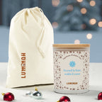 Candela Luminah Cime Innevate con sacchetto regalo in tessuto su sfondo natalizio.