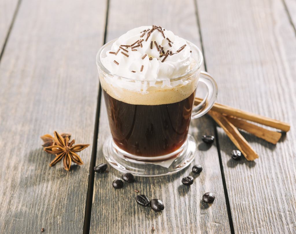 Tazza di caffè con panna, vaniglia e spezie su tavolo in legno.